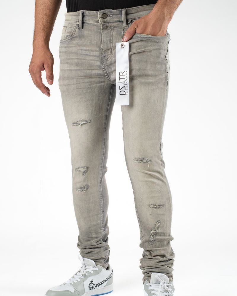 Person wearing light gray distressed jeans with a brand tag, standing against a white background