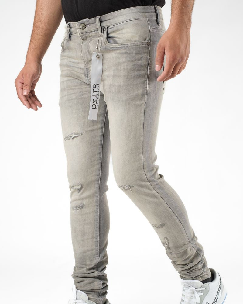 Person wearing light gray distressed jeans with a visible brand label on a white background