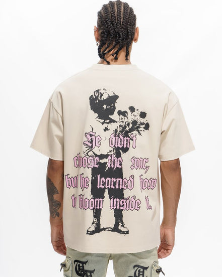 Person wearing a beige t-shirt with a graphic design and text on the back, standing against a white background.
