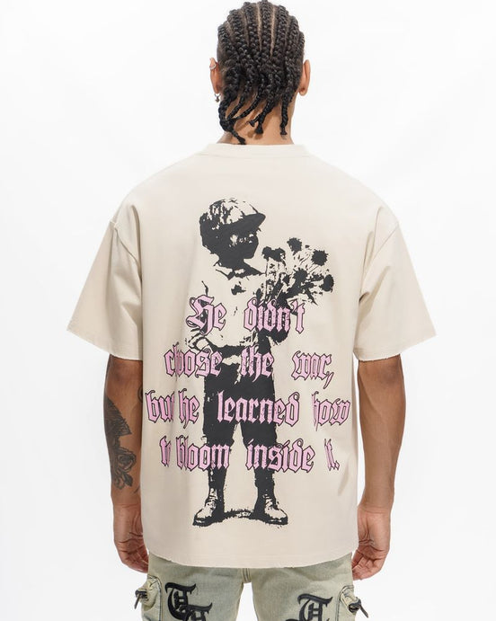 Person wearing a beige t-shirt with a graphic design and text on the back, standing against a white background.