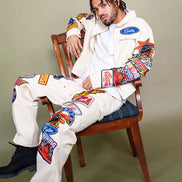 Person wearing a white outfit with colorful patches sitting on a wooden chair against a beige background