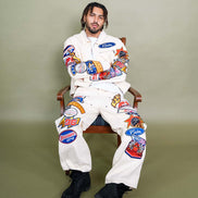Person wearing a white jumpsuit with colorful patches sitting on a chair against a plain background