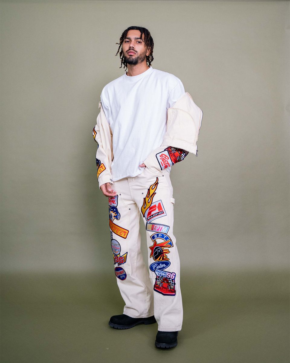 Person wearing a white outfit with colorful patches on a plain background