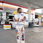 Person wearing a colorful jacket and pants with patches at a gas station.