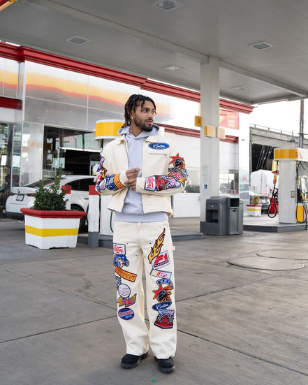 Person wearing a colorful jacket and pants with patches at a gas station.