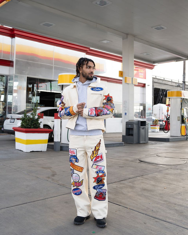 Person wearing a colorful jacket and pants with patches at a gas station.