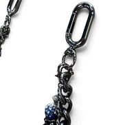 Close-up of a black metal chain accessory with a large carabiner-style clasp and dangling links, including two blue faceted beads near the bottom, on a white background.