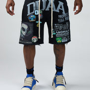 Person wearing black shorts with various graphics and text, standing against a white background