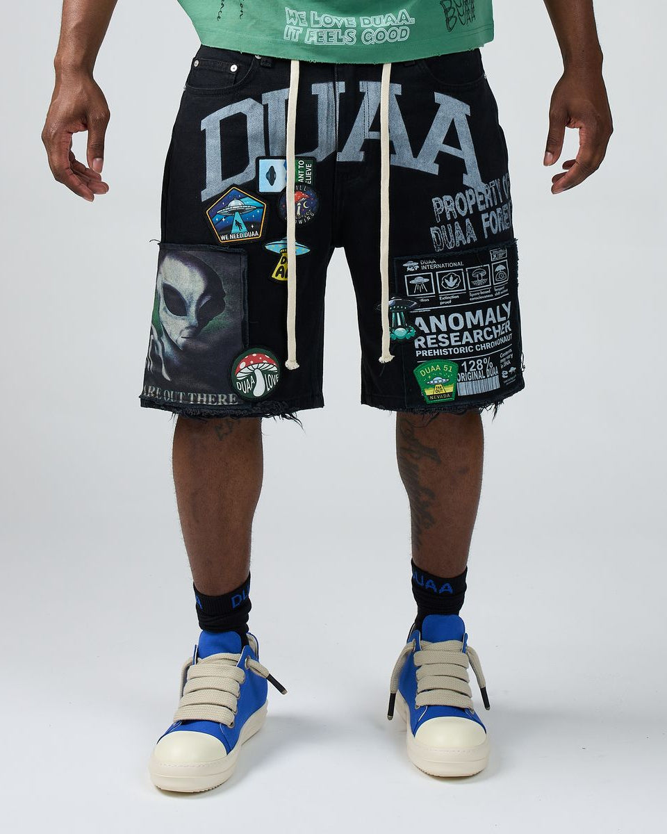 Person wearing black shorts with various graphics and text, standing against a white background