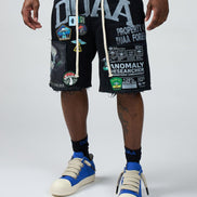 Person wearing black shorts with graphic designs and text, blue sneakers, and a green shirt on a white background.