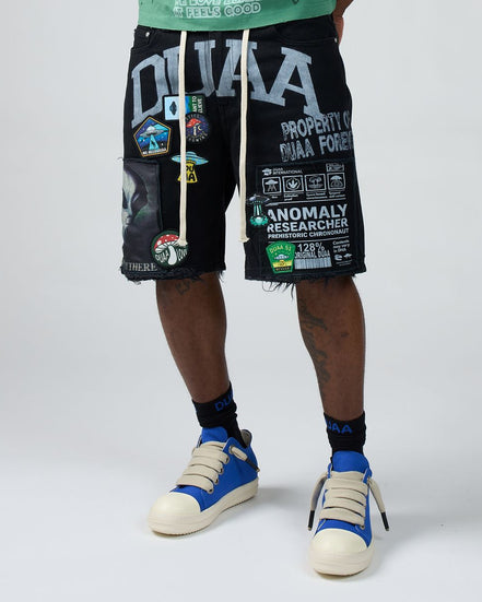 Person wearing black shorts with text and graphics, blue sneakers, and socks on a white background