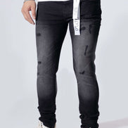 A person wearing slim-fit black distressed jeans with a faded gray wash, paired with white sneakers and a white t-shirt, shown from the waist down against a light gray studio background.