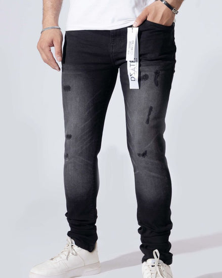 A person wearing slim-fit black distressed jeans with a faded gray wash, paired with white sneakers and a white t-shirt, shown from the waist down against a light gray studio background.