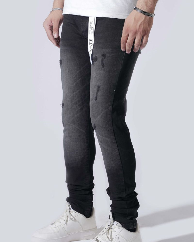 A person wearing slim-fit black distressed jeans with a faded gray wash at the thighs, paired with a white t-shirt and white sneakers, shown from the waist down on a light gray studio background.