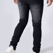 A person wearing slim-fit black denim jeans, a white t-shirt, and white sneakers, shown from the waist down against a light gray studio background.