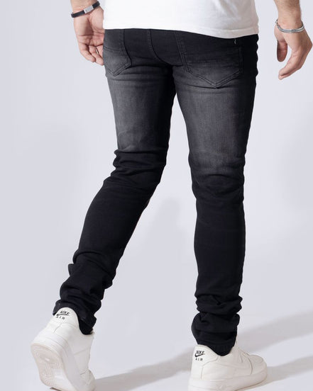A person wearing slim-fit black denim jeans, a white t-shirt, and white sneakers, shown from the waist down against a light gray studio background.