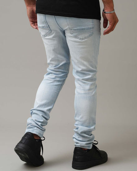 Person wearing light blue jeans and black shoes on a plain background