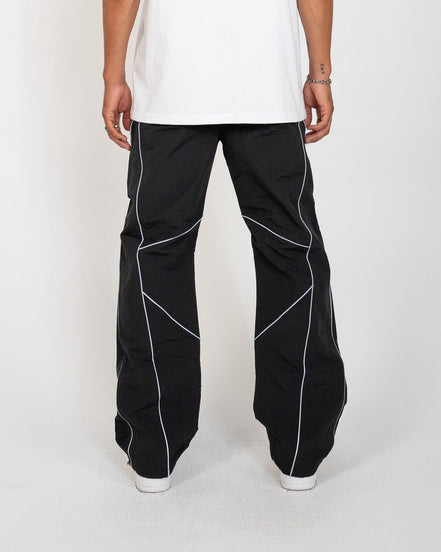 Black wide-leg pants with white geometric piping details, shown on a model from the back wearing a white t-shirt and white sneakers against a light gray background.