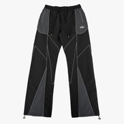 Black and gray geometric panel pants with a drawstring waist and zippered side pockets, shown flat against a light gray background.
