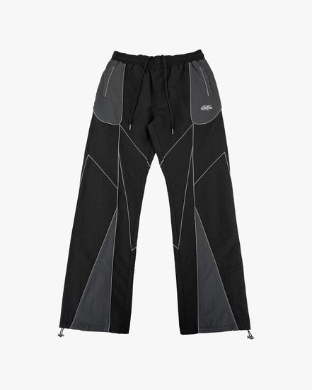 Black and gray geometric panel pants with a drawstring waist and zippered side pockets, shown flat against a light gray background.