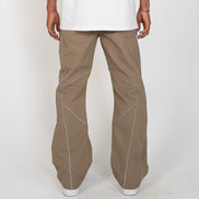A person shown from the back wearing loose-fit taupe-brown pants with contrasting light blue piping details, a white t-shirt, and white sneakers against a light gray studio background.