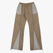 A pair of wide-leg pants in a taupe-beige color with contrasting light gray geometric paneling and a drawstring waist, shown against a plain light gray background.