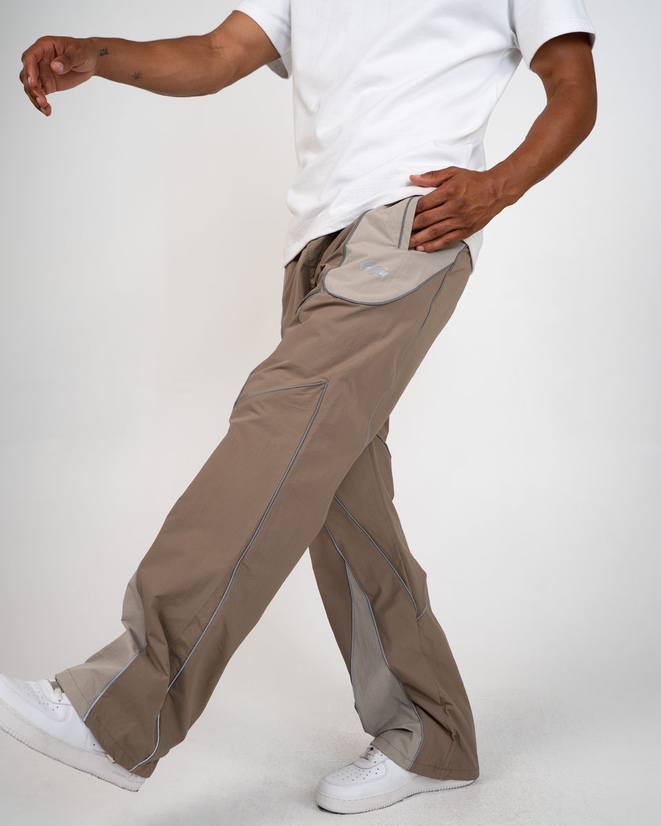 A person wearing loose-fit taupe-brown pants with contrast stitching and a white t-shirt, shown from the waist down in a studio setting.