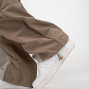 Close-up of a person wearing wide-leg taupe-brown pants and white low-top sneakers against a clean white studio background.