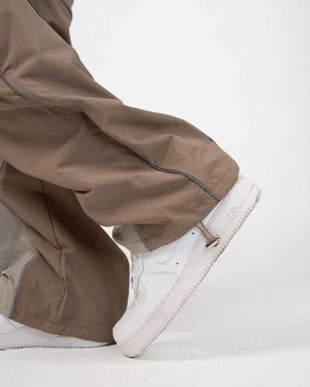 Close-up of a person wearing wide-leg taupe-brown pants and white low-top sneakers against a clean white studio background.