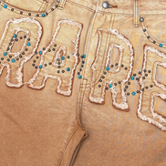 Brown pants with 'RARE' text in rhinestones on a beige background