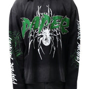 A person wearing a black long-sleeve graphic T-shirt with a large green and white 'PAPER' logo across the chest, white spider artwork, and white text down both sleeves, shown against a plain white background.