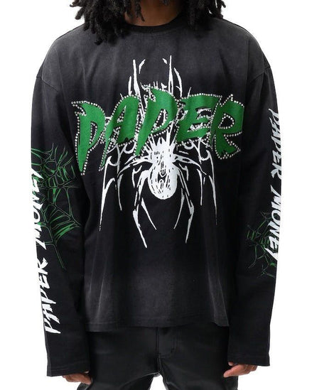 A person wearing a black long-sleeve graphic T-shirt with a large green and white 'PAPER' logo across the chest, white spider artwork, and white text down both sleeves, shown against a plain white background.