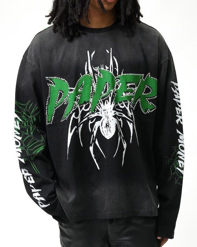 A person wearing a black long-sleeve graphic sweatshirt with a large green and white 'PAPER' spider design on the front, plus green and white text down both sleeves, against a plain white background.