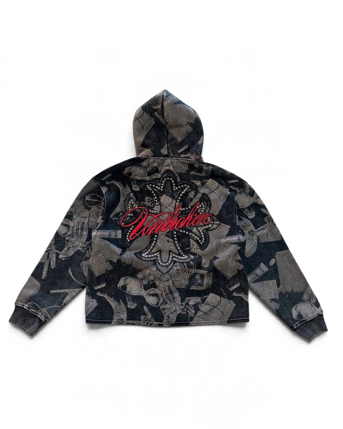 A cropped zip-up hoodie with a dark gray and black abstract collage print, featuring a large red 'Unbroken' script logo with rhinestone detailing on the back, shown against a plain white background.
