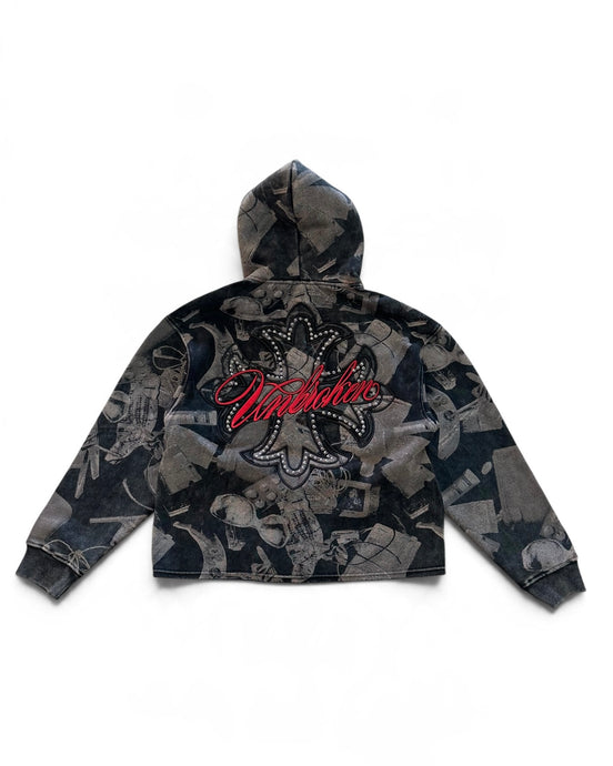 A cropped zip-up hoodie with a dark gray and black abstract collage print, featuring a large red 'Unbroken' script logo with rhinestone detailing on the back, shown against a plain white background.
