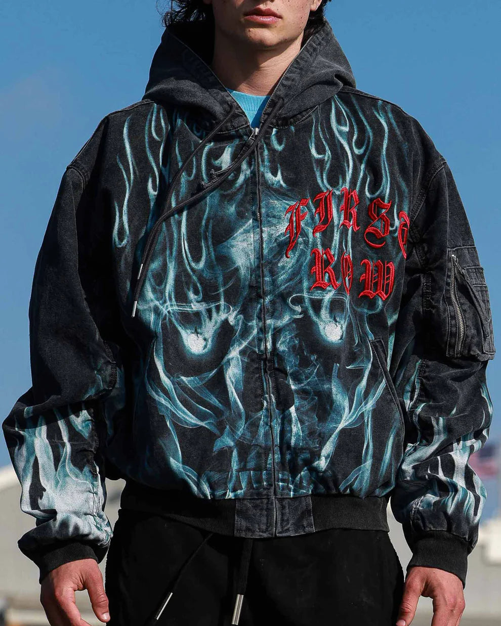 Person wearing a jacket with flame design and red text against a blue sky.