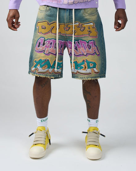 Person wearing denim shorts with colorful graphics and text, paired with yellow high-top sneakers on a white background.