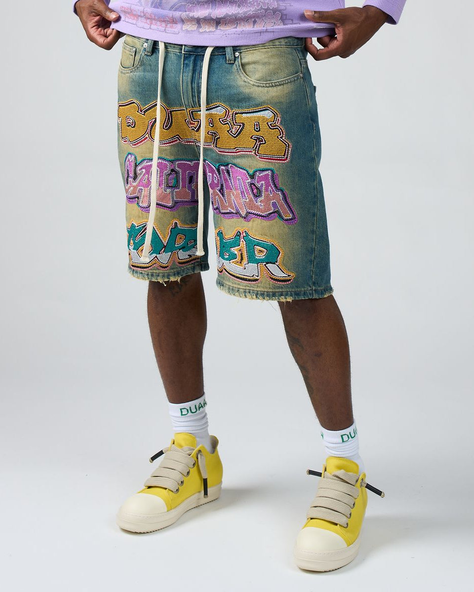 Person wearing denim shorts with colorful graphics and yellow sneakers on a white background