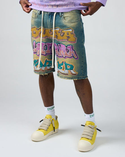 Person wearing denim shorts with colorful graphics and yellow sneakers on a white background