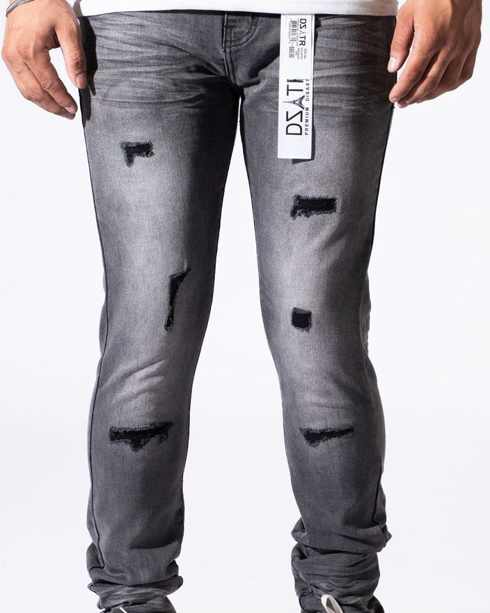 A person wearing distressed gray slim-fit jeans with ripped details and a white vertical brand tag on the thigh, paired with a white t-shirt and white sneakers against a white studio background.
