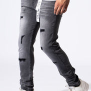 A person wearing faded dark gray distressed skinny jeans with ripped details, paired with a white t-shirt and white sneakers, shown from the waist down on a white studio background.