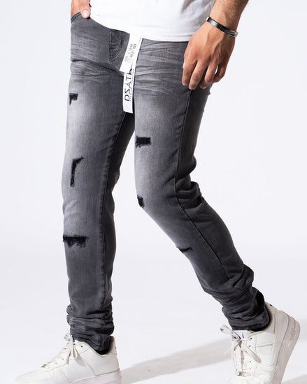 A person wearing faded dark gray distressed skinny jeans with ripped details, paired with a white t-shirt and white sneakers, shown from the waist down on a white studio background.