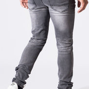 A person shown from the waist down wearing slim-fit gray jeans with a faded wash, paired with white sneakers and jewelry, against a plain white studio background.