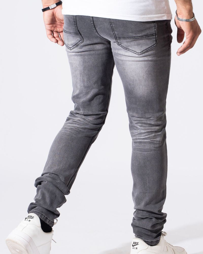 A person shown from the waist down wearing slim-fit gray jeans with a faded wash, paired with white sneakers and jewelry, against a plain white studio background.