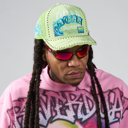 Person wearing a bright green cap with text and graphics, red sunglasses, and a pink sweatshirt with graphic designs.