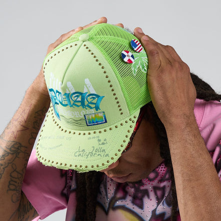 Person holding a green cap with various logos and text against a neutral background