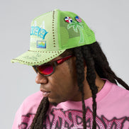 Person wearing a green cap with text and flags, pink sunglasses, and a pink shirt with black text.