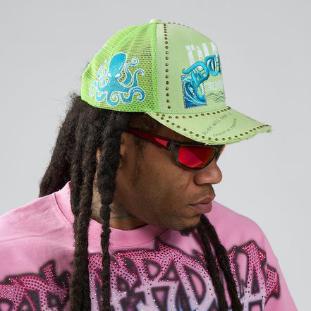 Person wearing a green cap with blue designs and red sunglasses, against a gray background