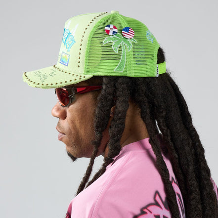 Person wearing a bright green cap with palm tree design and colorful pins, on a plain background