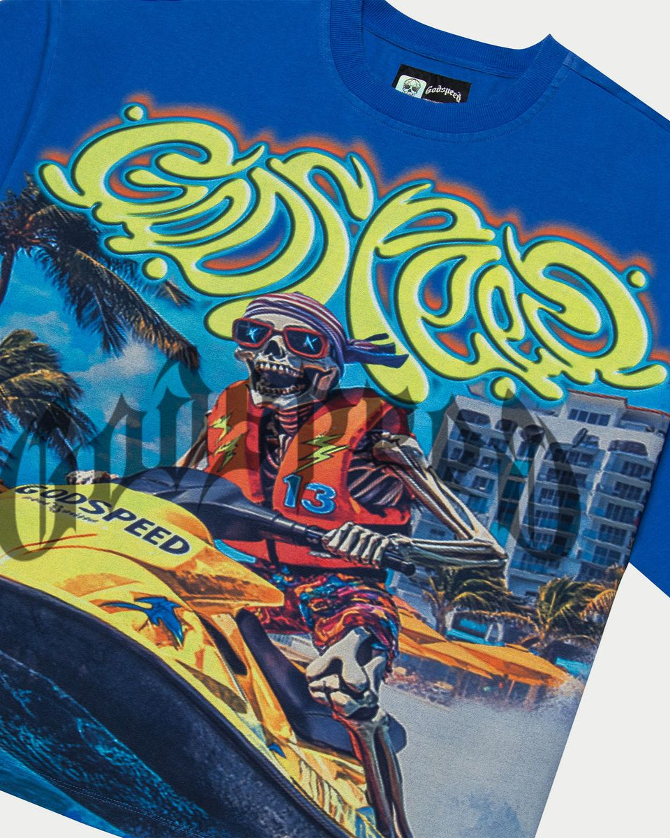Blue t-shirt with a colorful graphic of a skeleton on a jet ski, palm trees, and buildings.